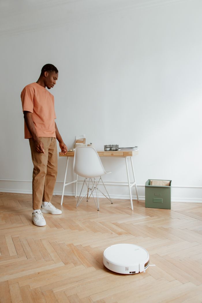 Man in casual attire looking at robot vacuum in a modern home office setting.